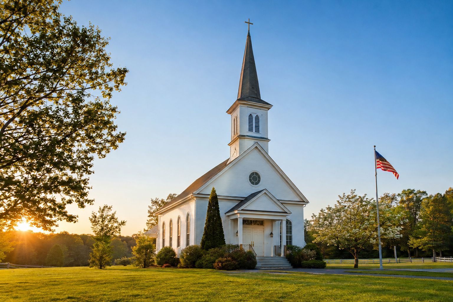 A white steeple church at sunset with an American flag