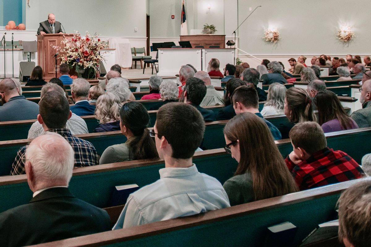 A congregation seated in pews during a service, pastor at the pulpit
